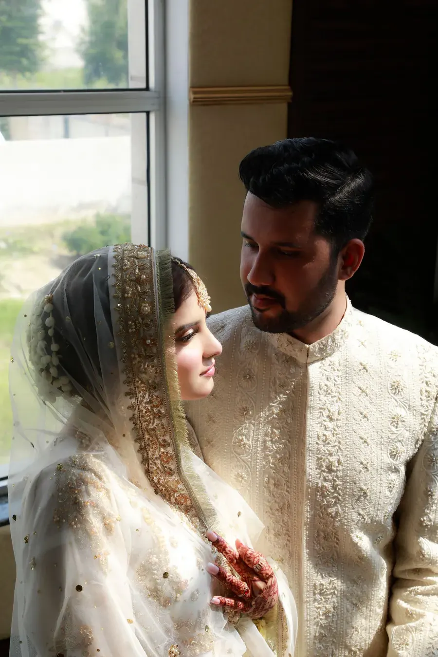 A bride and groom in traditional clothes by a window